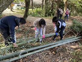 切り出した竹をノコギリで切る学生