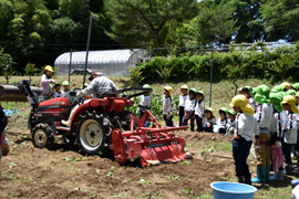 耕うん機に乗る長友用務員の説明を聞く園児たち