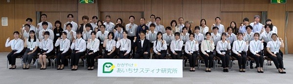 開所式にて、所長の大村知事、パートナー企業担当者、ファシリテーターと一緒に記念撮影<br>　
最前列右から１人目チームmeijoに参加の小川舞子さん（理科専修3年）<br>右から４人目チームNiterraに参加の江口穂乃里さん（社会専修2年）
